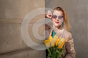 Woman holding yellow tulips, leaning against stone wall. Women& x27;s holiday concept, giving flowers.