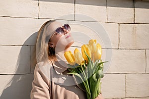 Woman holding yellow tulips, leaning against stone wall. Women& x27;s holiday concept, giving flowers.