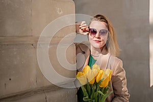 Woman holding yellow tulips, leaning against stone wall. Women& x27;s holiday concept, giving flowers.