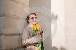 Woman holding yellow tulips, leaning against stone wall. Womens holiday concept, giving flowers.