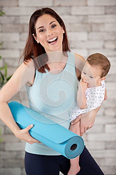 woman holding young baby and rolled up yoga mat