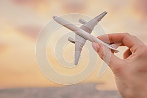 Woman holds an airplane model in her hand in the background sky during sunset. Close-up view.