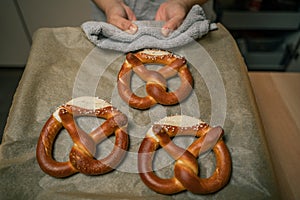Woman holds baking tray with baked pretzels in hand