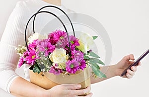 A woman holds a basket with flowers and a smartphone in her hands. Floristry, delivery from a flower shop