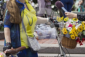 Woman holds bicycle, basket with flowers. Hand holds a microphone. Interview. Frame part