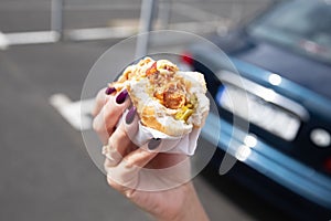 A woman holds a bitten hot dog in her hand.