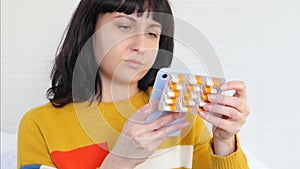 A woman holds a blister with pills in her hand while making a purchase in an online pharmacy using an app on her