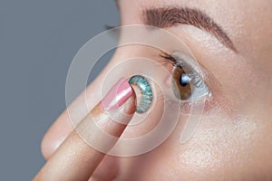 Woman holds a blue contact lens on her finger.