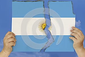 Woman holds in both hands against a blue sky torn in two cardboard with seared edges depicting the national flag, the concept of