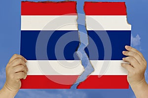 Woman holds in both hands against a blue sky torn in two cardboard with seared edges depicting the national flag, the concept of