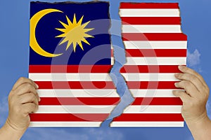 Woman holds in both hands against a blue sky torn in two cardboard with seared edges depicting the national flag of Malaysia, the