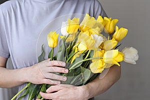 A woman holds a bouquet of beautiful yellow tulips in her hands.