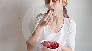 woman holds bowl with strawberry and eats berries