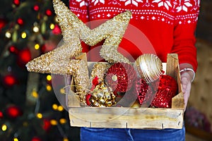 A woman holds a box with a lot of Christmas decorations