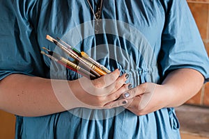 A woman holds brushes in her hands for drawing with watercolors. Hobby art concept. Close-up selective focus.