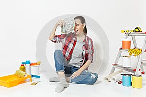 Woman holds bundle of dollars, cash money, sits on floor with instruments for renovation apartment isolated on white