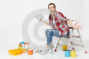 Woman holds bundle of dollars, cash money, sits on ladder with instruments for renovation apartment isolated on white