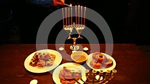 A woman holds a candle in her hand that lights candles in a Hanukkah candlestick. a woman lights candles from the first candle fro