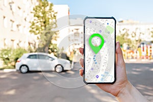 A woman holds a cellphone with an online map app, hand close-up. In the background is a city street with car. The concept of