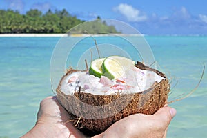 Woman holds Ceviche Dish served in a coconut shell against a isl