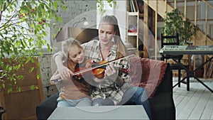 A woman holds a child's hand with a bow and helps to play the violin