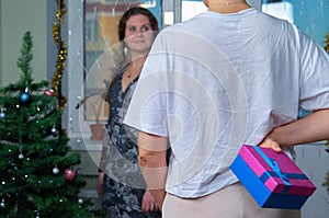 A woman holds a Christmas present behind her back before giving it to another woman