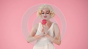 Woman holds colorful lollipop, kisses it, and licks it with pleasure. Woman in the image of Marilyn Monroe in studio on