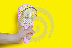 A woman holds a comb brush with fallen hair after combing on a yellow background