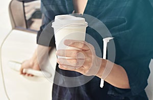 Woman holds a cup of coffee standing in front of her car