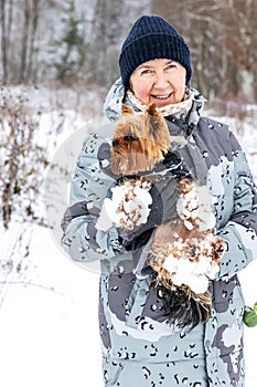 A woman holds a dog covered in snow in her arms in a winter forest