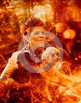 A woman holds a dog in front of a blazing fire, channeling the essence of an fire sorceress in a mystical forest. photo