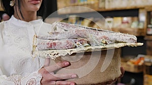 A woman holds a dry homemade sausage on a tray in a healthy organic food store.