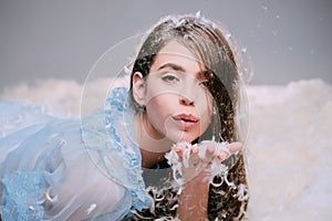 Woman holds feathers in hand and blow. Female model in transparent blue nightie lay on bed. Girl on calm face lay on bed