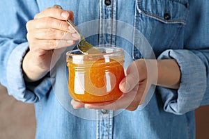 Woman holds glass jar with orange jam close up