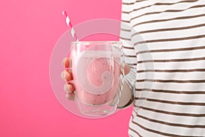 Woman holds glass strawberry milkshake against pink background