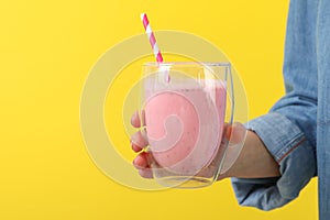 Woman holds glass strawberry milkshake against yellow background