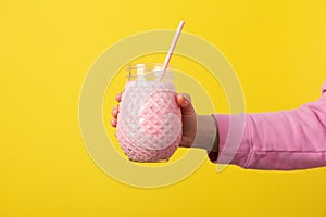 Woman holds glass strawberry milkshake on yellow background