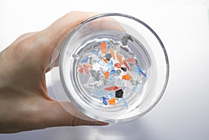 A woman holds a glass of water with pieces of plastic in her hand.