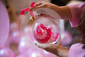 A woman holds a glass watering can with pink bows against a background of pink balloons.