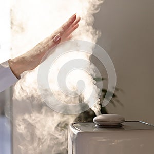 Woman holds hand over steam aroma oil diffuser on the table at home, steam from the air humidifier
