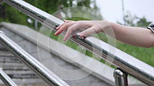 Woman holds hand on wet metal railing, water drops dripping down her fingers.