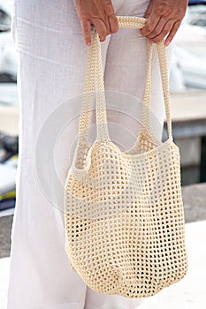 Woman holds a handmade beige knitted bag in her hand near her legs outdoors. Sustainable shopping. Wasteless lifestyle
