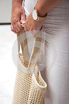 Woman holds a handmade beige knitted bag in her hand near her legs outdoors. Sustainable shopping. Wasteless lifestyle