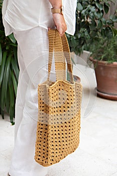 Woman holds a handmade beige knitted bag in her hand near her legs outdoors. Sustainable shopping. Wasteless lifestyle