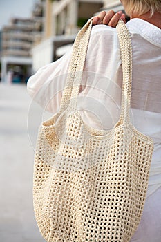 Woman holds a handmade beige knitted bag outdoors. Sustainable shopping. Wasteless lifestyle