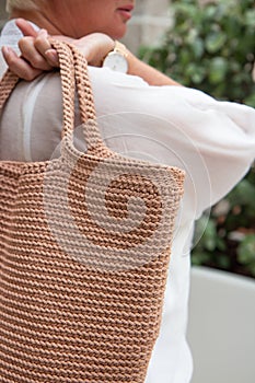 Woman holds a handmade beige knitted bag outdoors. Sustainable shopping. Wasteless lifestyle