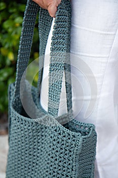 Woman holds a handmade blue knitted bag outdoors. Sustainable shopping. Wasteless lifestyle