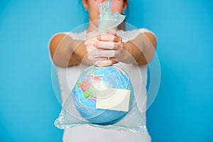 Woman holds in hands plastic bag empty sticker and planet earth at blue background.