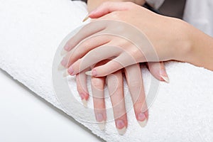 Woman holds hands on towel for manicure treatment procedure in spa salon. Beautiful hands of young woman close-up on towel.