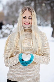 A woman holds a heart made of snow in her hands in a winter park